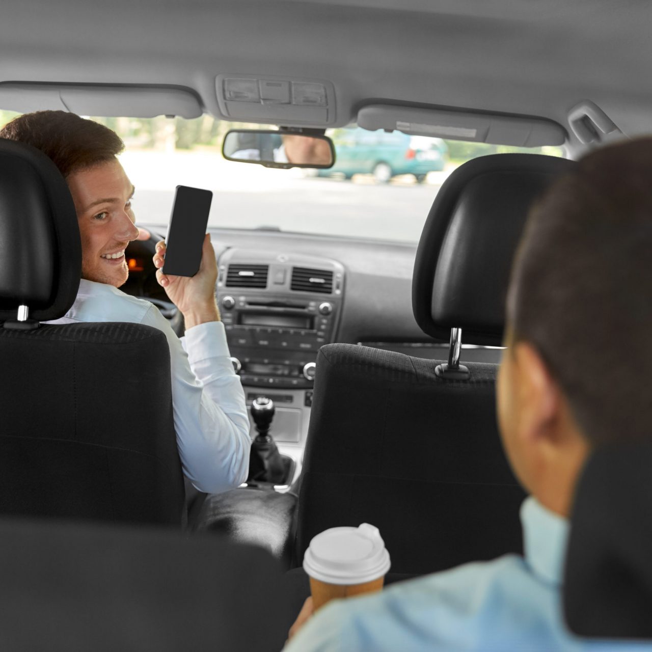 transportation, taxi and technology concept - smiling car driver showing smartphone to male passenger